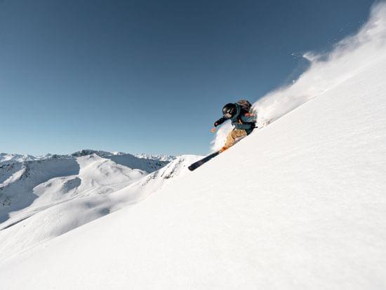 Freestyle skier carving through fresh powder on a steep snowy mountain slope