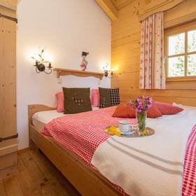 Gemütliches Alpenzimmer mit Holzmöbeln, rot kariertem Bett und einem Tablett mit Kaffee und Blumen