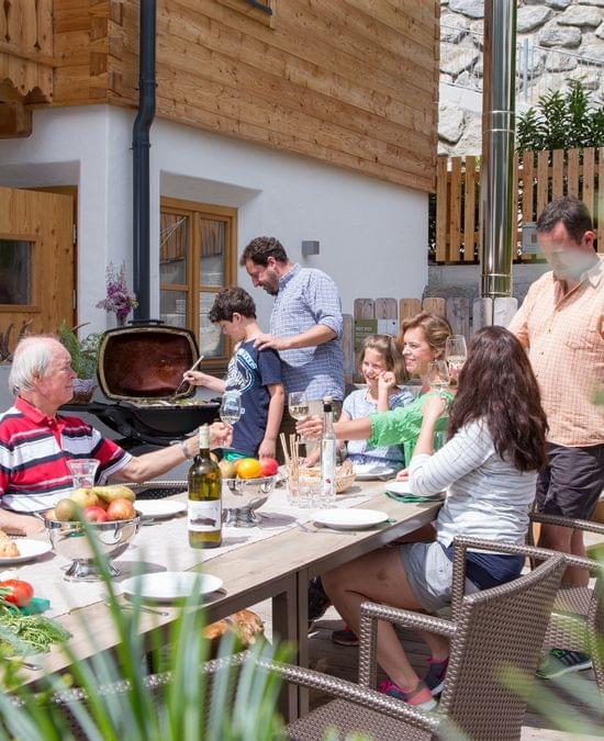 Familie genießt Grillabend auf sonniger Terrasse vor Holzchalet