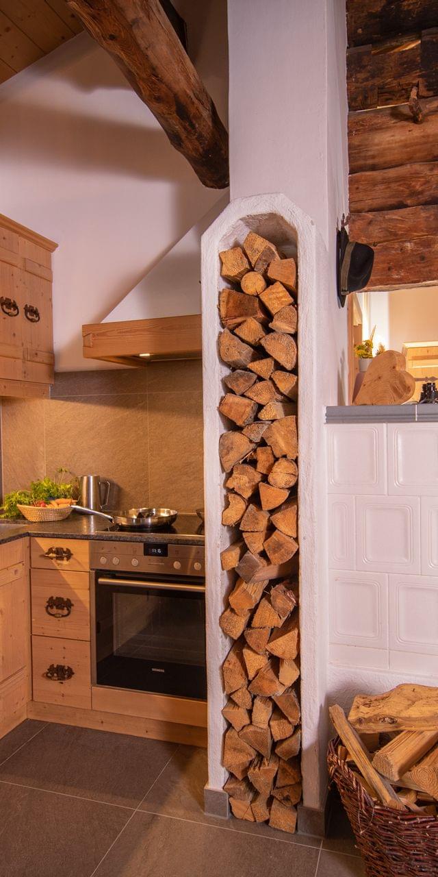 Gemütliche rustikale Küche mit Holzmöbeln, Brennholzstapel und traditionellem Ofen