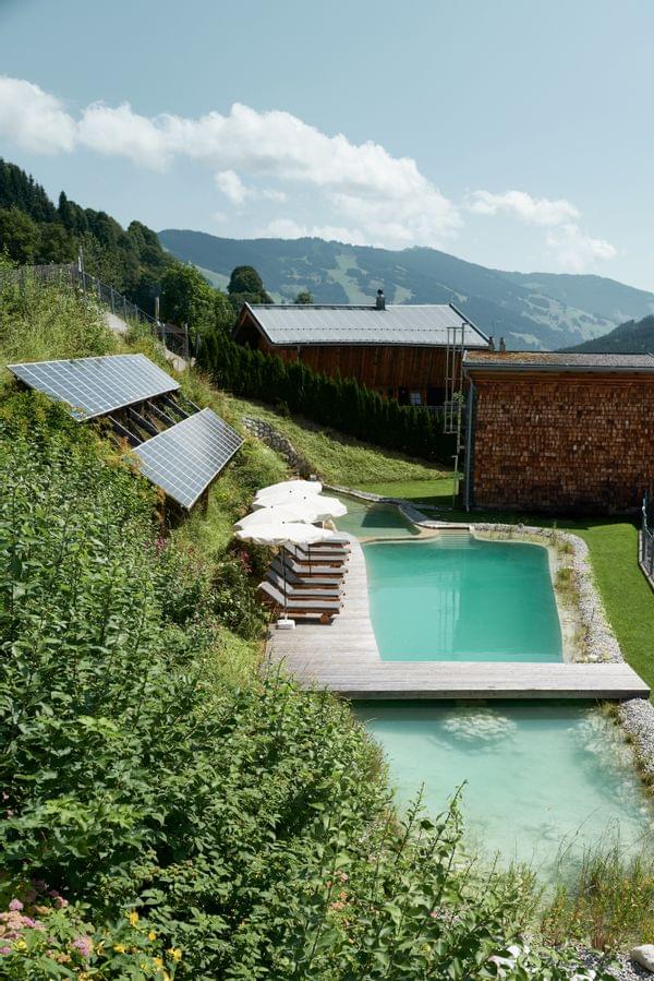 Umweltfreundlicher Naturpool mit Liegen und Solarpanels in alpiner Berglandschaft