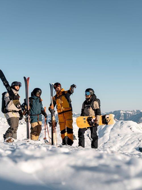 Gruppe von Skifahrern und Snowboardern mit Ausrüstung auf verschneitem Berg mit Alpenpanorama