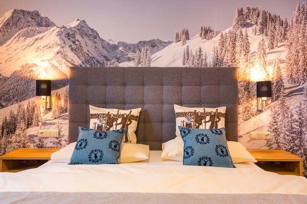 Cozy double hotel bed with alpine-themed pillows and snowy mountain wall mural