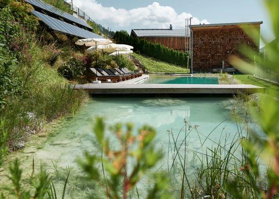 Ökohotel mit natürlichem Badeteich, Solarpanels, Liegen und Sonnenschirmen in grüner Hanglage