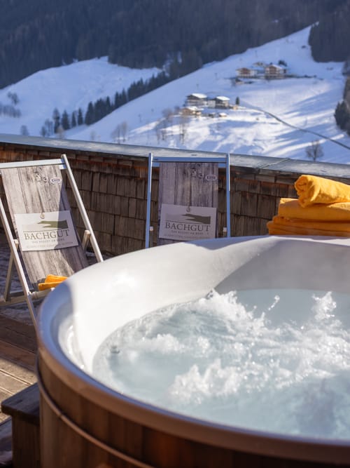 A hot tub with lounge chairs beside it, with snow-covered mountains and sunshine in the background.