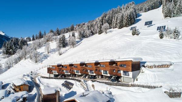 Moderne Holzchalets in verschneitem Alpen-Skigebiet mit bewaldetem Berghang