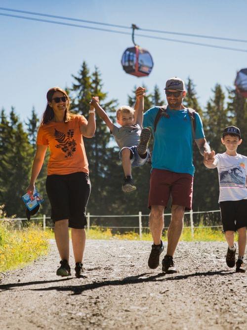Happy family hiking on mountain trail with cable cars in background