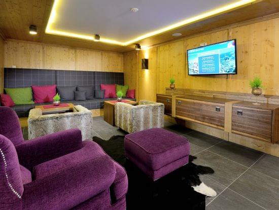 Gemütliche Alpenlounge mit lila Sesseln, fellbezogenen Hockern und Wandfernseher