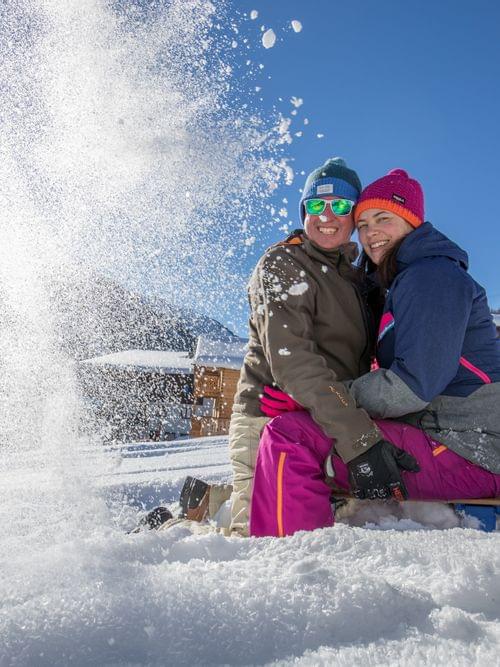 Smiling couple in colorful winter clothes sitting on a sled in snowy mountain village
