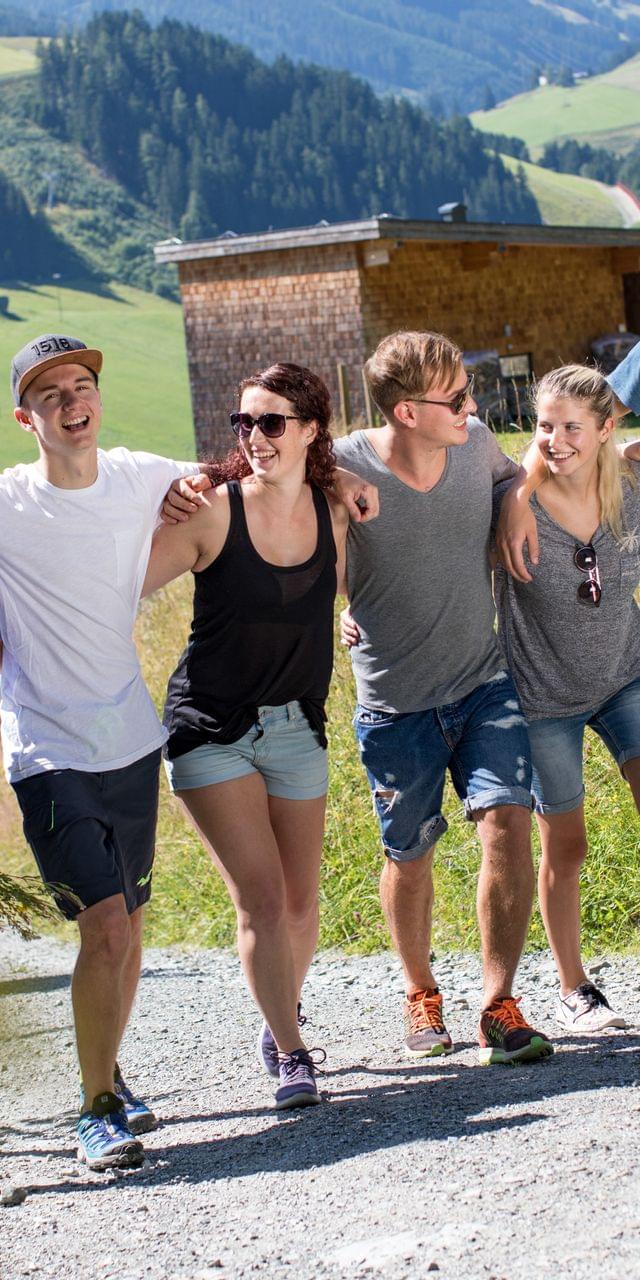 Gruppe junger Freunde wandert gemeinsam bei Sonnenschein auf einem Bergweg im Sommer