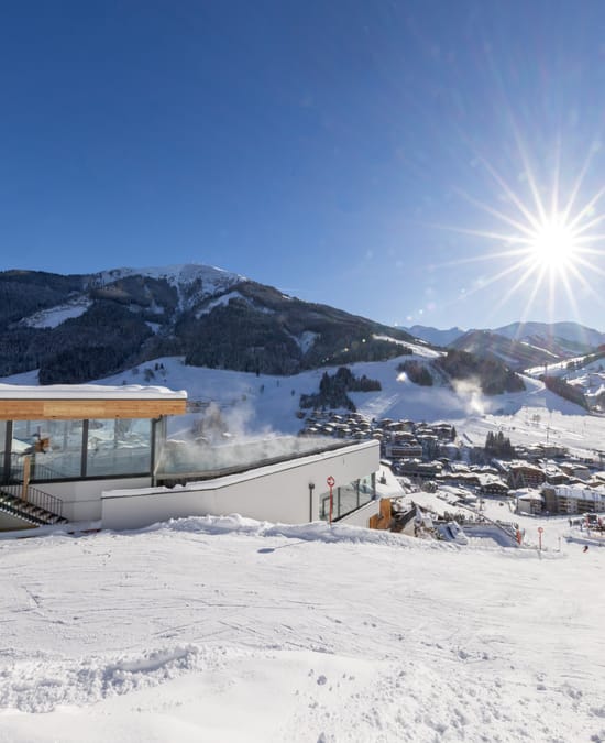 Ausblick auf das Badehaus und das Ortszentrum von Hinterglemm, gleich neben der Skipiste. Winterlich verschneit und Sonnenschein