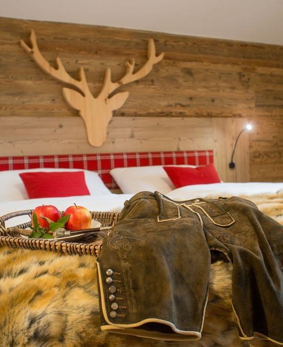 Gemütliches Alpenhotelzimmer mit Pelzdecke, Lederhose, Äpfeln und rustikaler Holzeinrichtung
