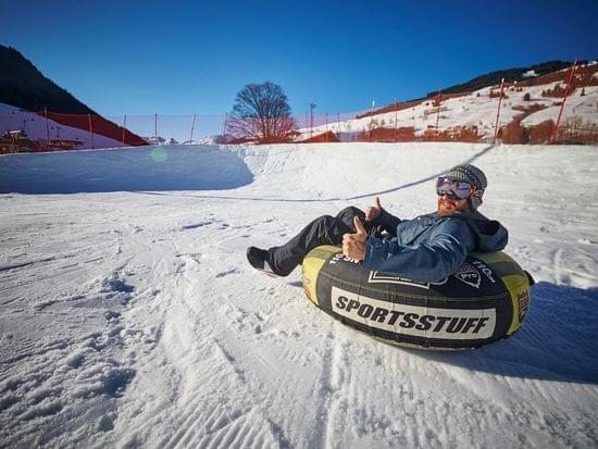 Man snow tubing on a sunny day in the mountains giving thumbs up