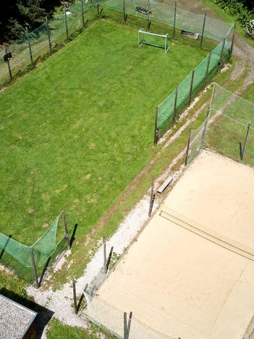 Aerial view of fenced grass soccer field and sand volleyball court in a forested area