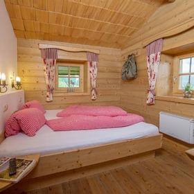 Cozy alpine bedroom with wooden walls, red checkered bedding and rustic curtains