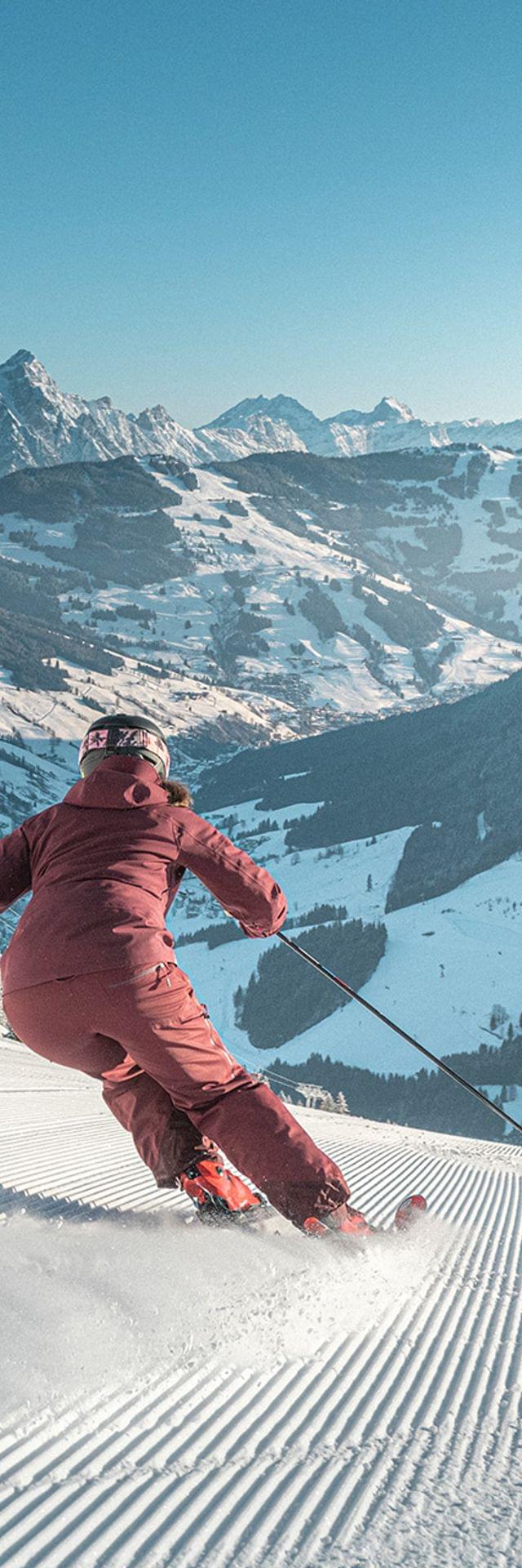 Skifahrer fährt bei Sonnenschein eine frisch präparierte Piste in den österreichischen Alpen hinunter