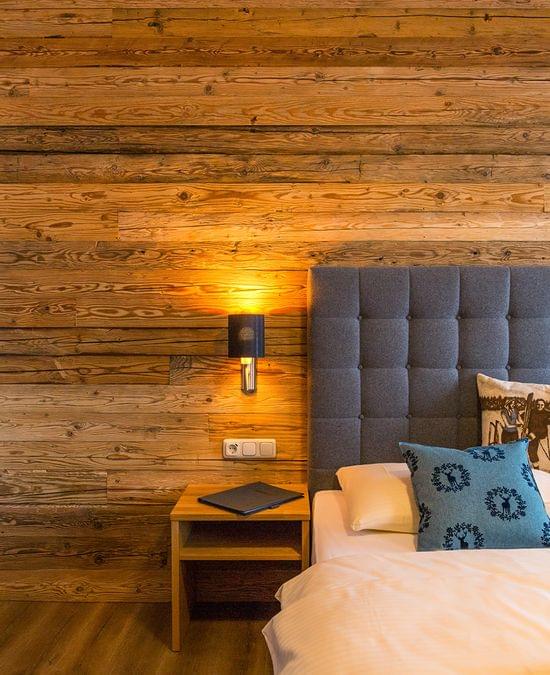 Cozy hotel room with wooden wall, grey upholstered bed, and bedside table with lamp