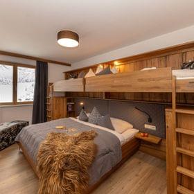 Cozy alpine hotel room with double bed and wooden bunk beds in winter setting
