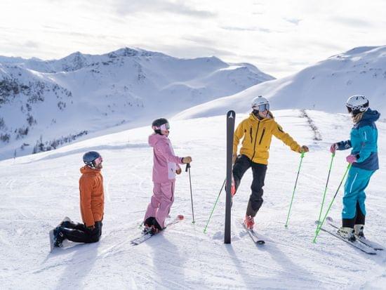 Group of skiers in colorful outfits talking on snowy mountain slope in sunny alpine setting