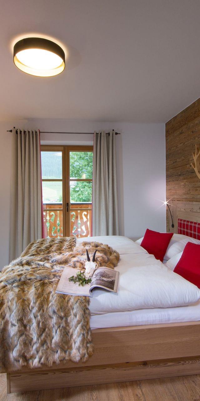 Gemütliches Alpenhotelzimmer mit Holzeinrichtung, roten Akzenten und Felldecke auf Doppelbett