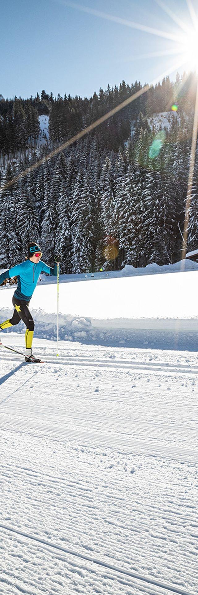 Cross-country skier gliding on groomed snowy trail in mountain landscape under bright sun