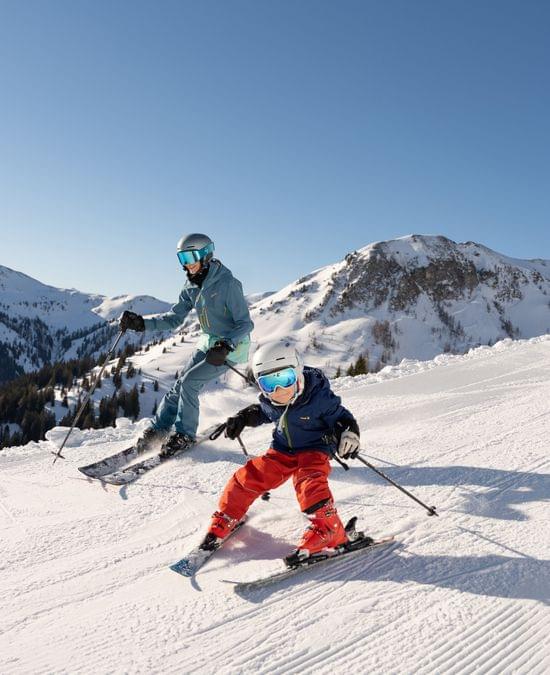 Family skiing downhill on groomed slope in sunny alpine mountain resort
