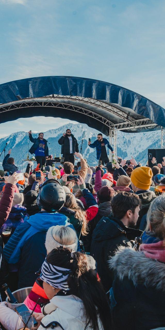 Eine Festivalbühne mit vielen Leuten davor, im Hintergrund die Berge und Schnee 