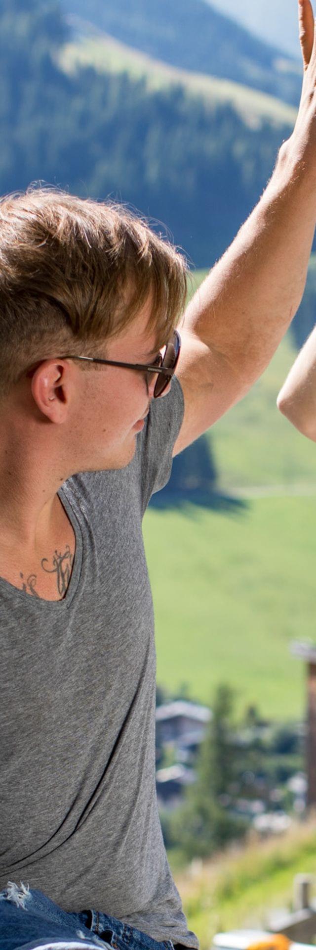 Zwei junge Männer geben sich ein High Five an einem sonnigen Tag in den Bergen