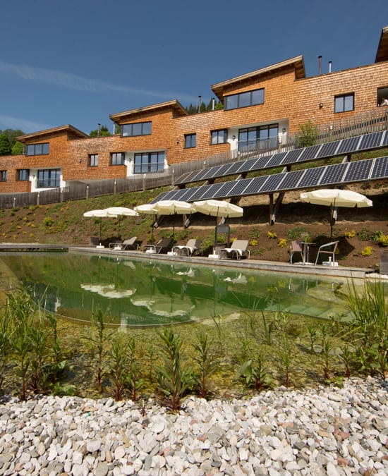 A view of the natural swimming pond and the Bachgut chalets clad in wood.