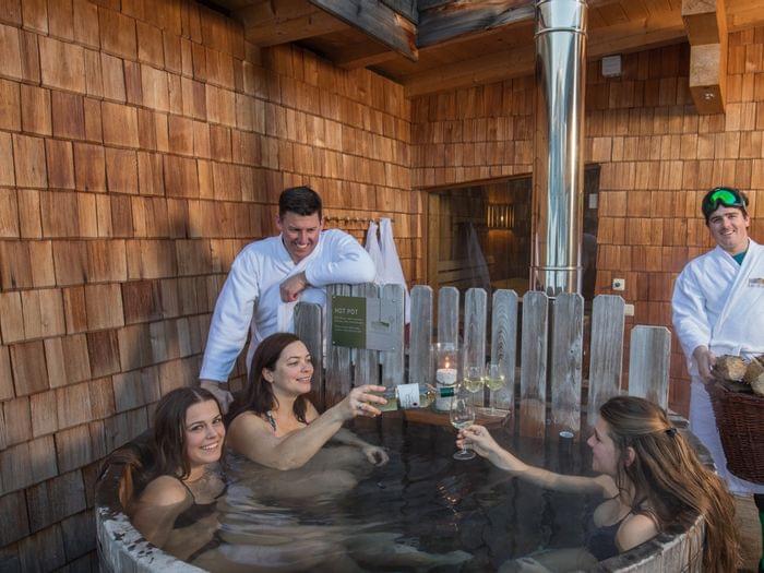 Group enjoying hot tub with wine on wooden deck at mountain wellness resort