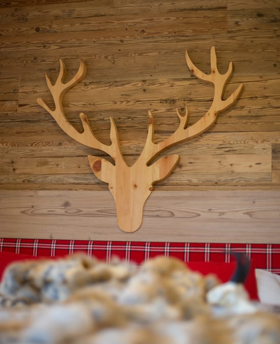 A wooden wall with a wooden antler decoration, with a faux fur blanket in the foreground.
