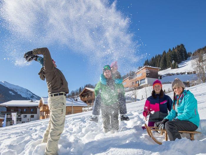 Group enjoying winter vacation in snowy alpine village with sleds and playful snow throwing