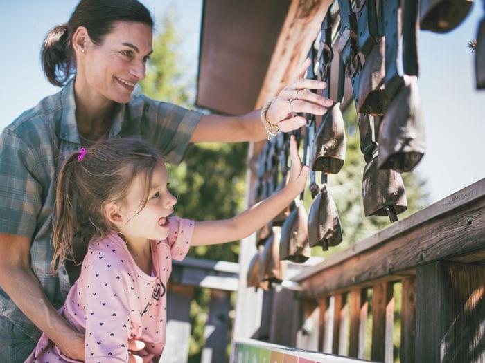 Mother and daughter playing with hanging cowbells at outdoor nature park