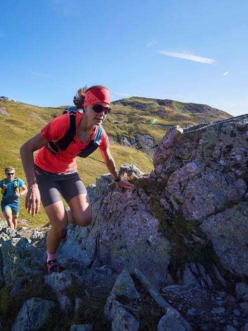 Trail runners climbing rocky mountain ridge under clear blue sky