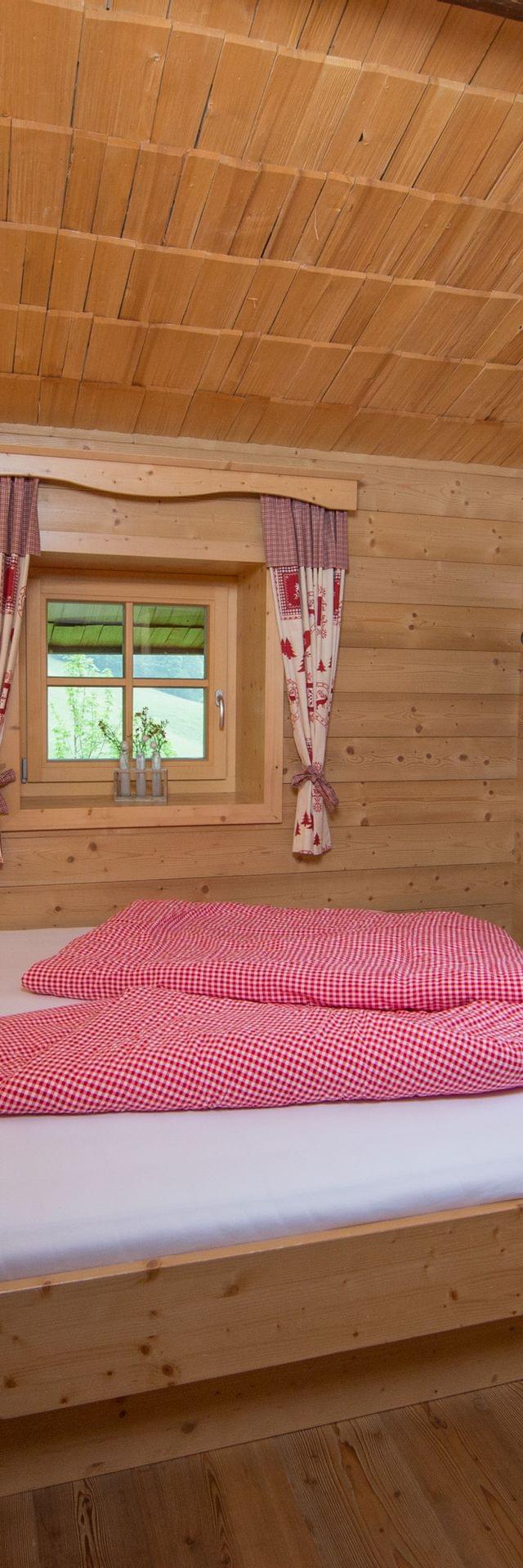 Gemütliches alpines Holzschlafzimmer mit rotkarierter Bettwäsche und traditionellen Vorhängen
