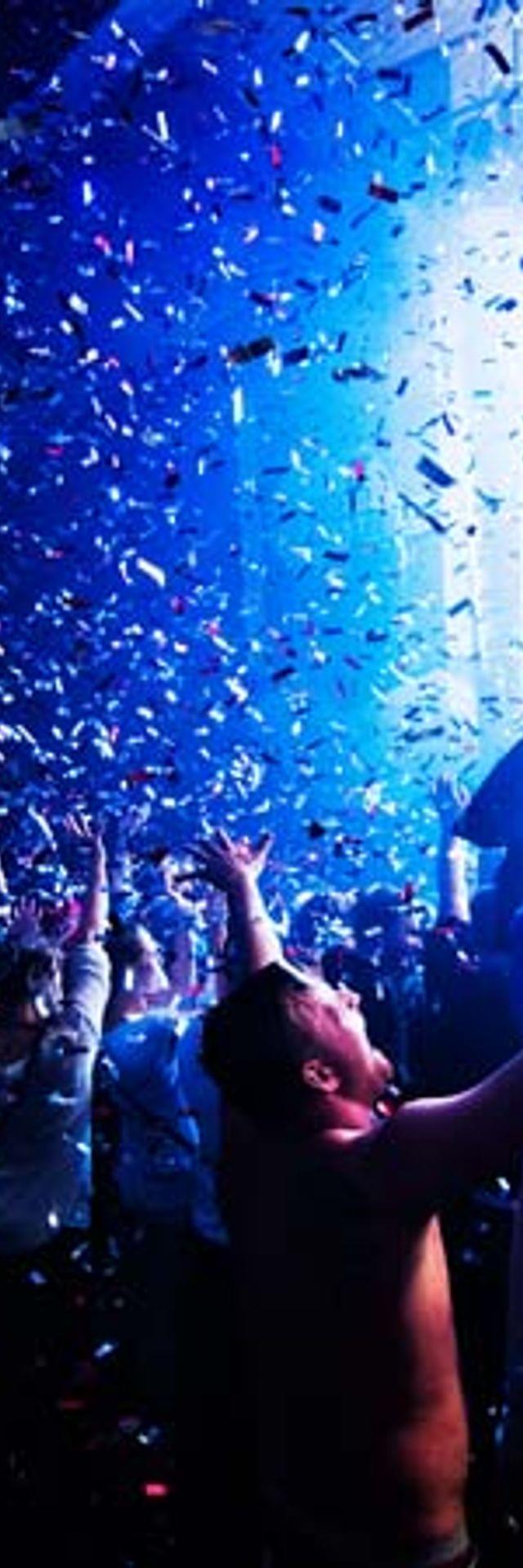 Crowd dancing at night club with confetti and colorful lights during music festival