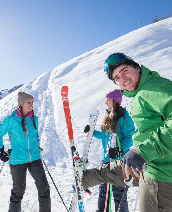 Group of friends in colorful ski gear preparing on a sunny day in the snowy mountains