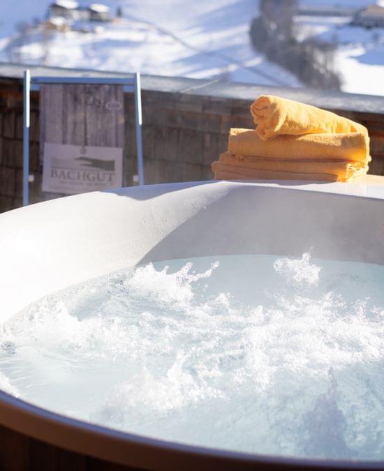 Blubbernde Whirlwanne auf der Terrasse mit Liegestühlen, im Hintergrund Winterlich Verschneite Landschaft 
