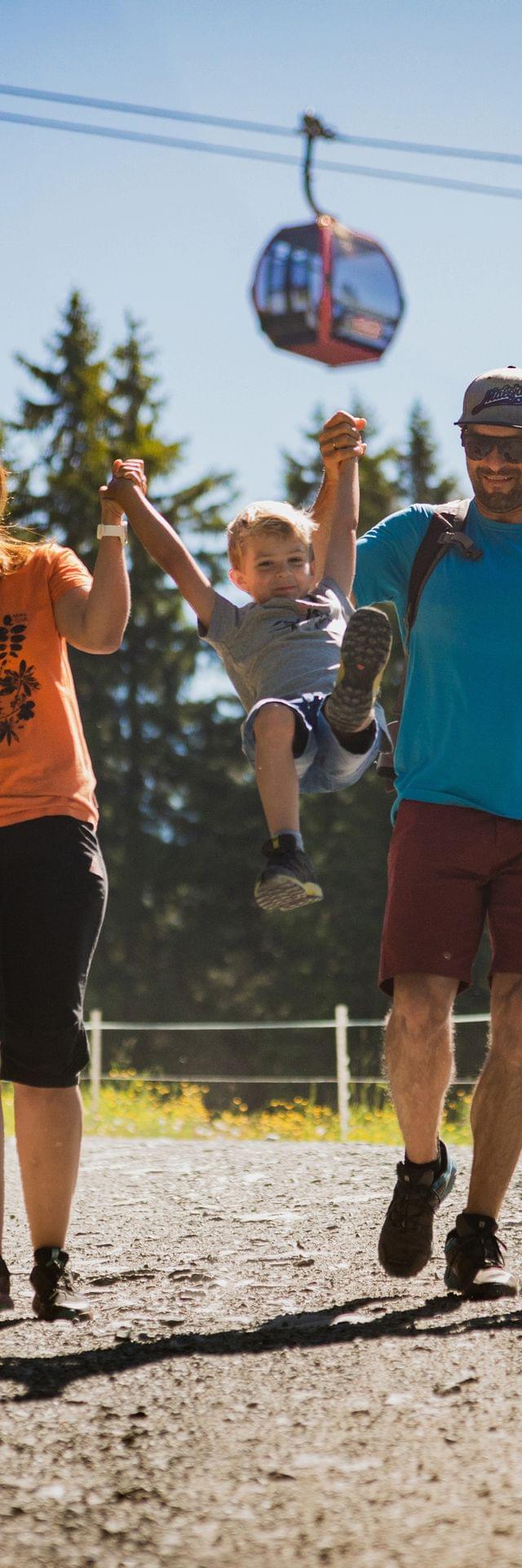 Happy family hiking on a sunny mountain trail with gondolas in the background