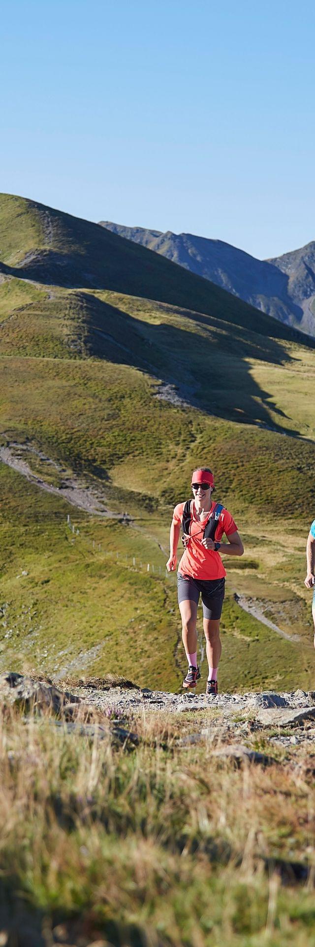 Trail runners on a mountain ridge path with alpine peaks in the background