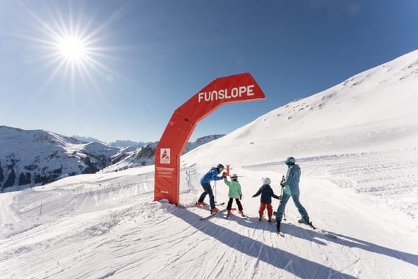 A family with two children skiing, standing by an arch marking the Snow Trail.