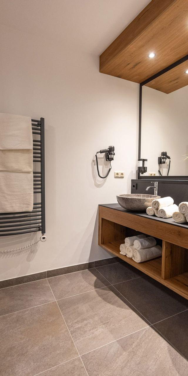 Modernes Spa-Badezimmer mit Steinausguss, gerollten Handtüchern und Holzakzenten