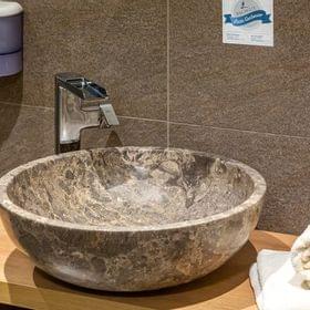 Modernes Bad mit steinernem Waschbecken, Chromarmatur und gerollten weißen Handtüchern