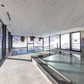 The Bachgut bathhouse with a children’s indoor pool and a swimming pool that leads outside into the infinity pool, with a deeply snow-covered winter landscape in the background.