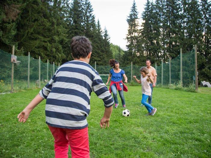 Family playing soccer on grass field surrounded by trees