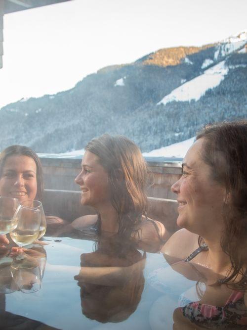 Drei Frauen entspannen mit Wein im Whirlpool eines verschneiten Bergresorts