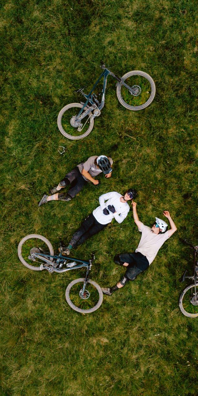 3 Biker mit ihren Bikes in der Wiese liegend, genießen einen Sommertag 