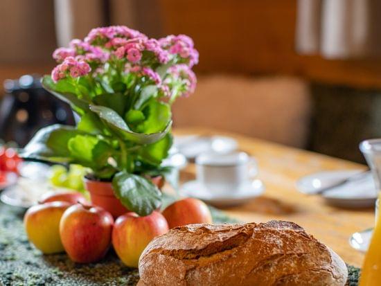 Rustic breakfast table with fresh bread, apples, flowers, and coffee cups