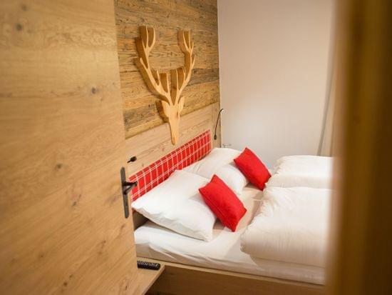 Gemütliches Hotelzimmer mit Doppelbett, roten Kissen und Wanddeko aus Holzgeweih