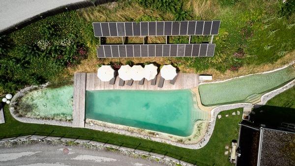 Vogelperspektive von Bachgut Naturbadeteich, Rundherum mit Liegen und Sonnenschirmen und ein Teil der Photovoltaik Anlage 